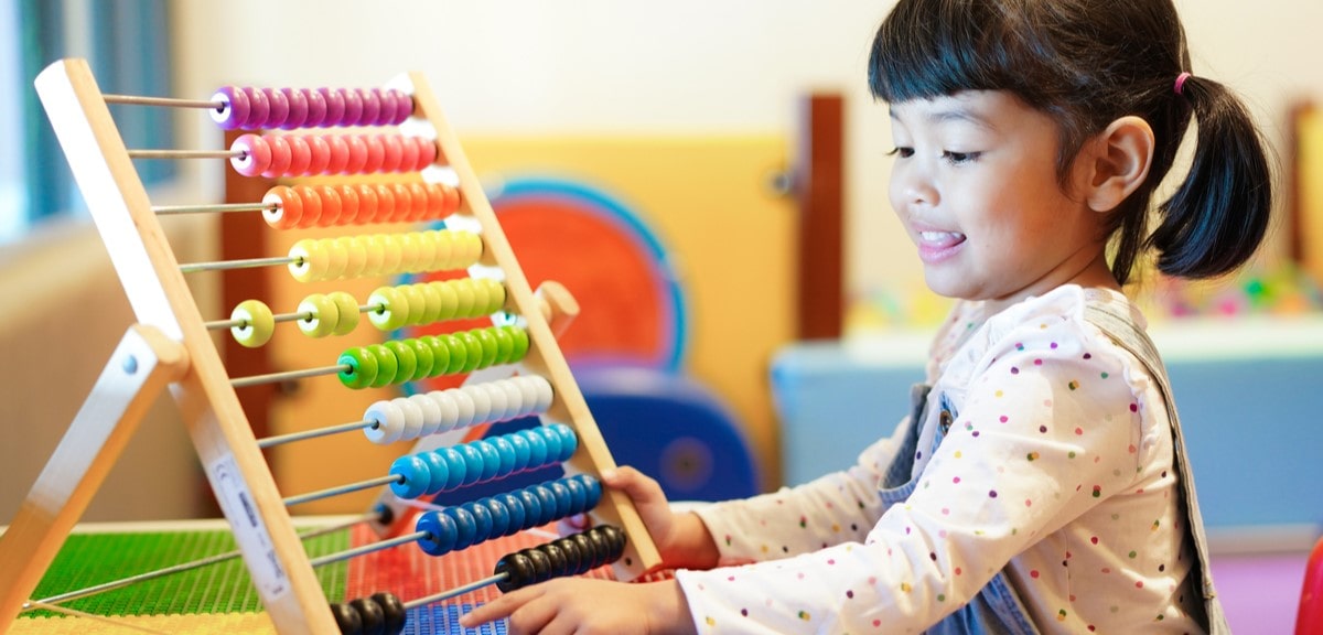 Young child playing with a colourful abacus, smiling and engaged in a hands-on maths activity