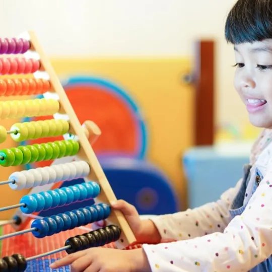 Young child playing with a colourful abacus, smiling and engaged in a hands-on maths activity