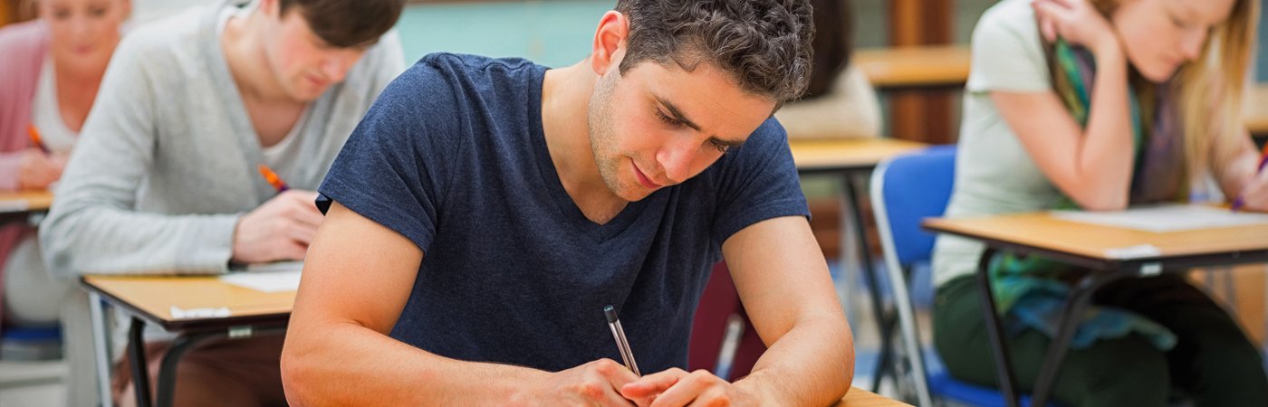 Male student concentrating on exam paper in a classroom setting.
