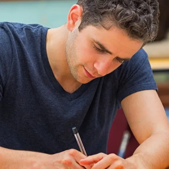 Male student concentrating on exam paper in a classroom setting.