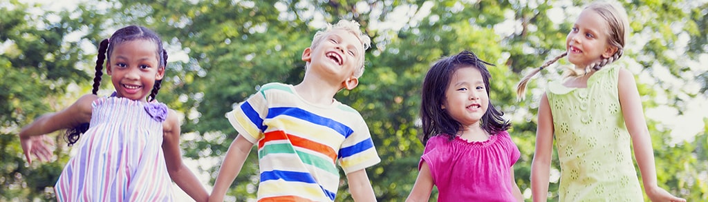 Four smiling children holding hands and jumping in the air, enjoying outdoor playtime together