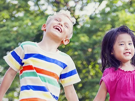 Four smiling children holding hands and jumping in the air, enjoying outdoor playtime together