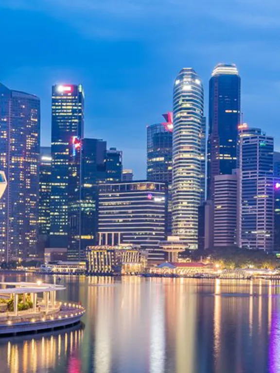 A landscape view of a Singaporean skyline at dusk. with the river lit up by city lights.