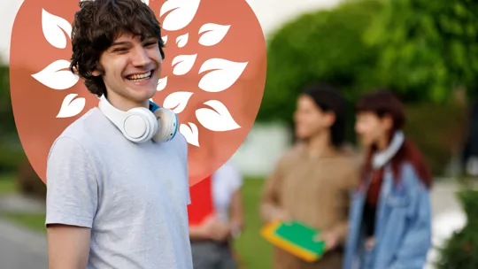 A young person with headphones around their neck smiling broadly, with other blurred individuals and greenery in the background.