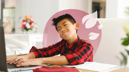 A young student with a pensive expression, typing on a laptop at a desk with an open notebook.