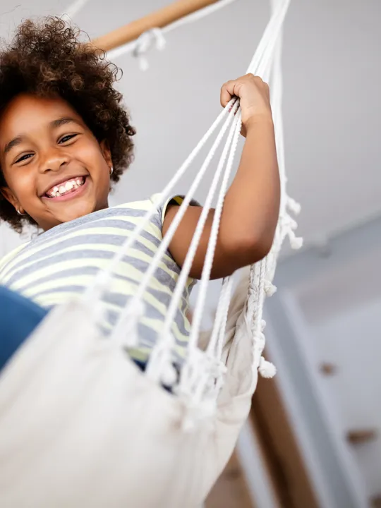 Happy child relaxing in a hammock at home, smiling confidently at the camera.