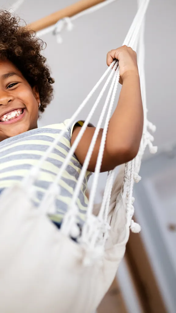 Happy child relaxing in a hammock at home, smiling confidently at the camera.