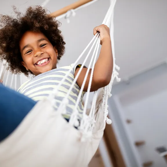 Happy child relaxing in a hammock at home, smiling confidently at the camera.