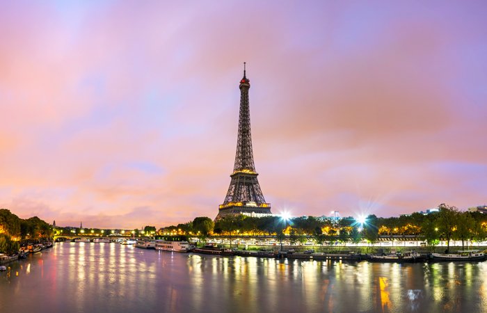 Eiffel Tower illuminated at dusk, reflected in the River Seine under a pastel sky in Paris.