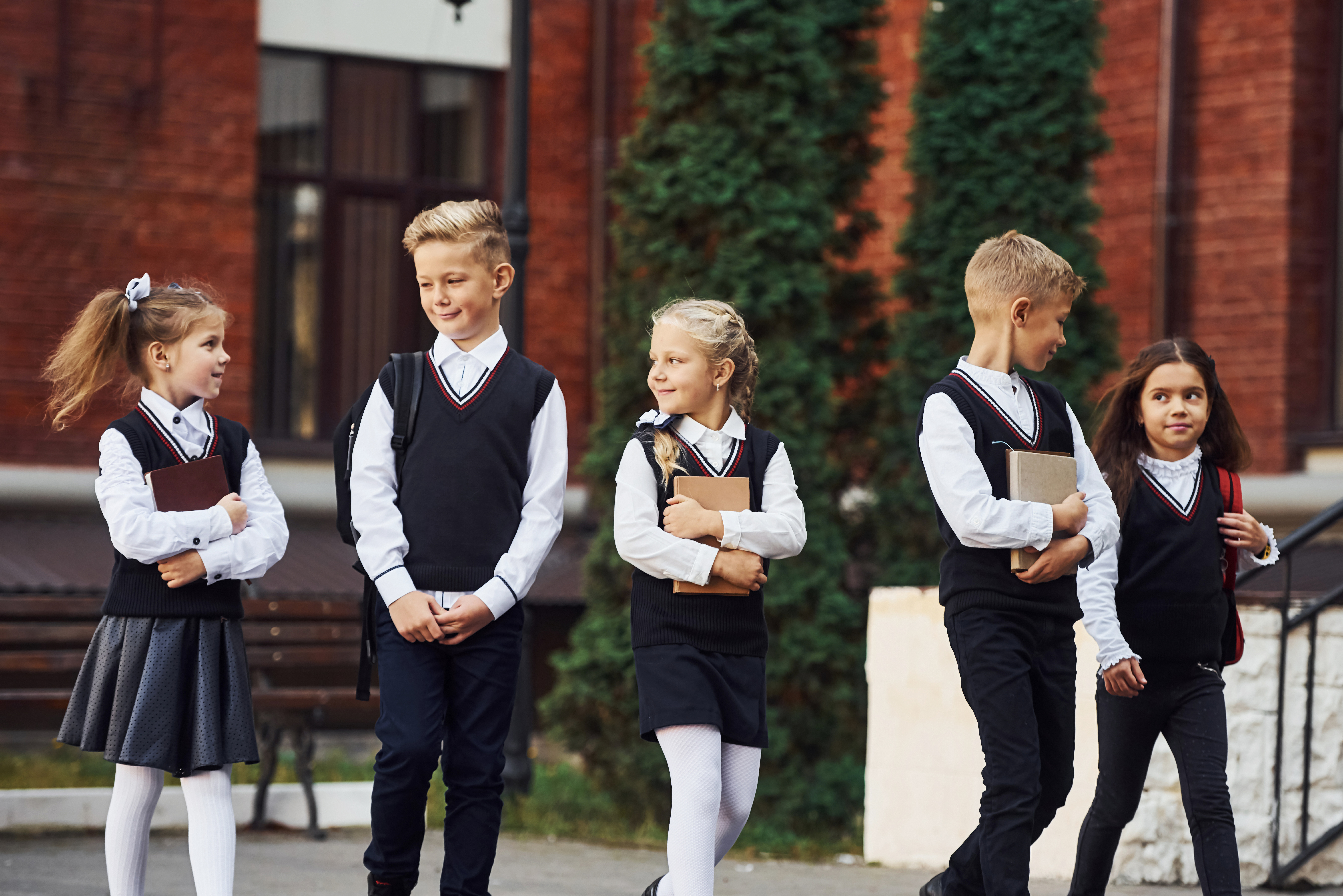 Group of five young students in smart private school uniforms, holding books outdoors, representing the traditional schooling environment that homeschooling serves as a great alternative to.