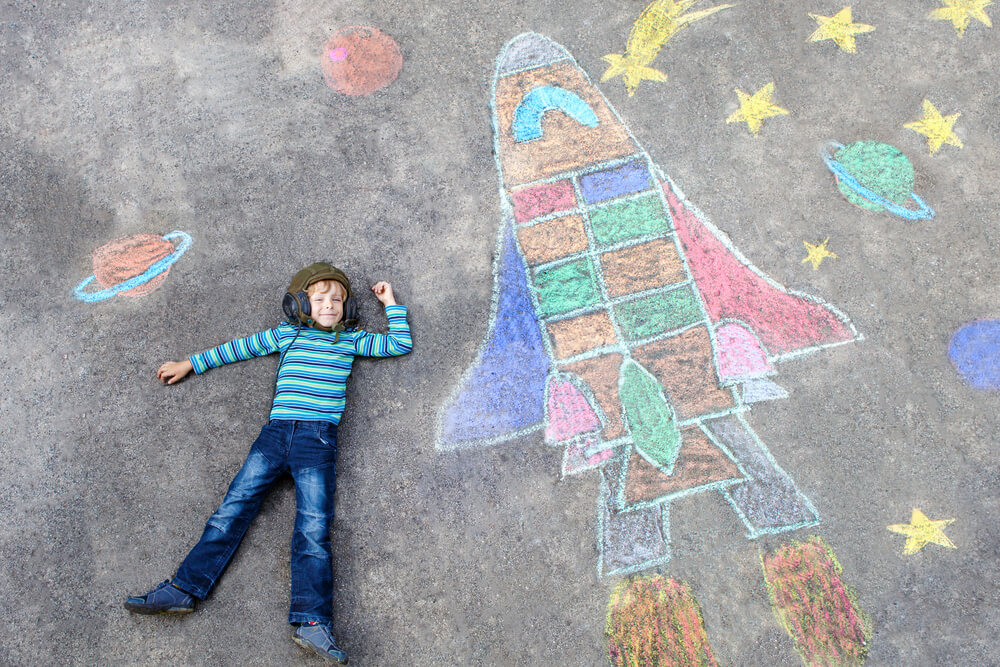 Young child laid down next to colourful chalk art.