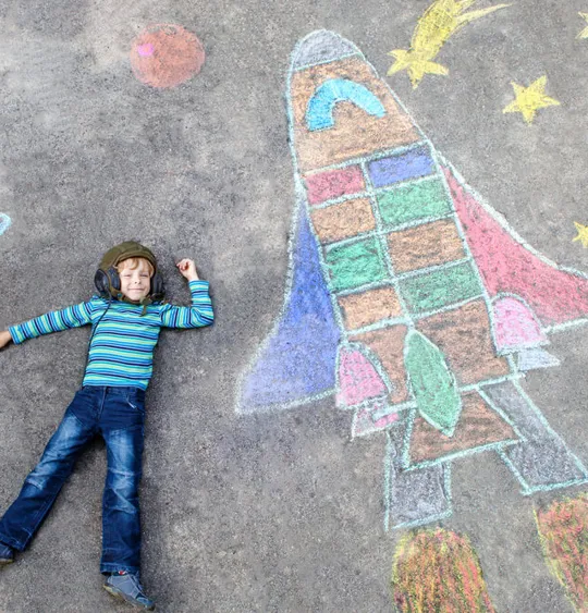 Young child laid down next to colourful chalk art.