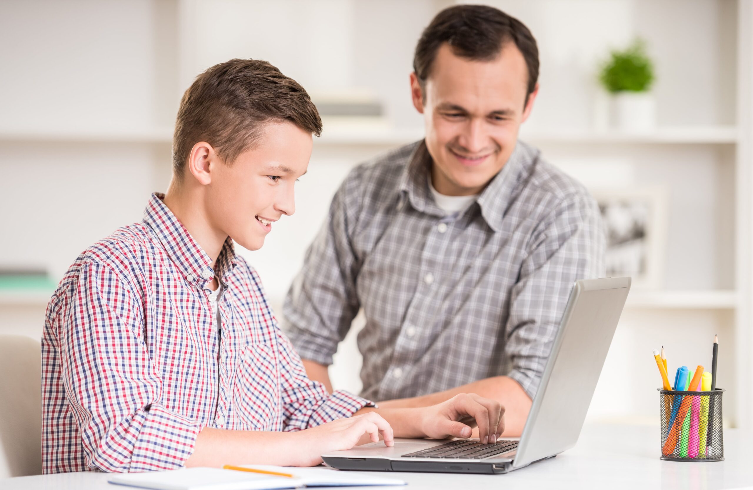 Parent supporting teenage son with online learning at home, highlighting personalised homeschooling support