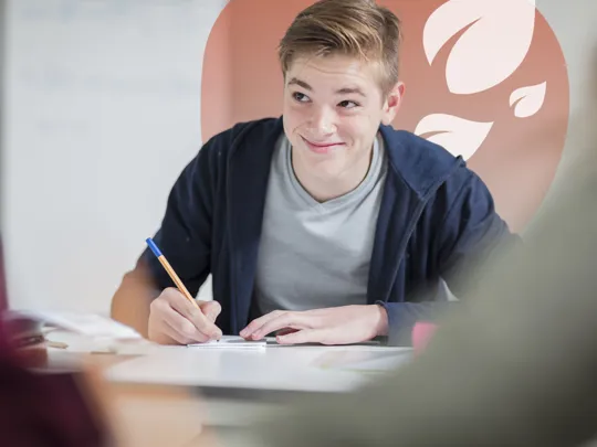 Teenage boy in casual clothing smiling while writing in a notebook during study.