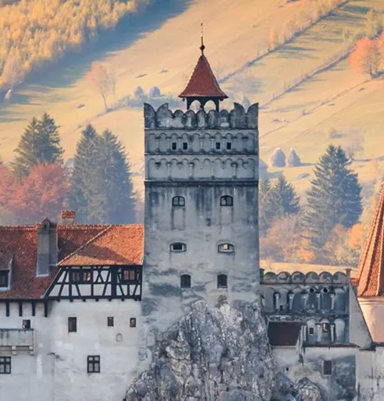 A landscape view of a Romanian castle in the middle of the country side.