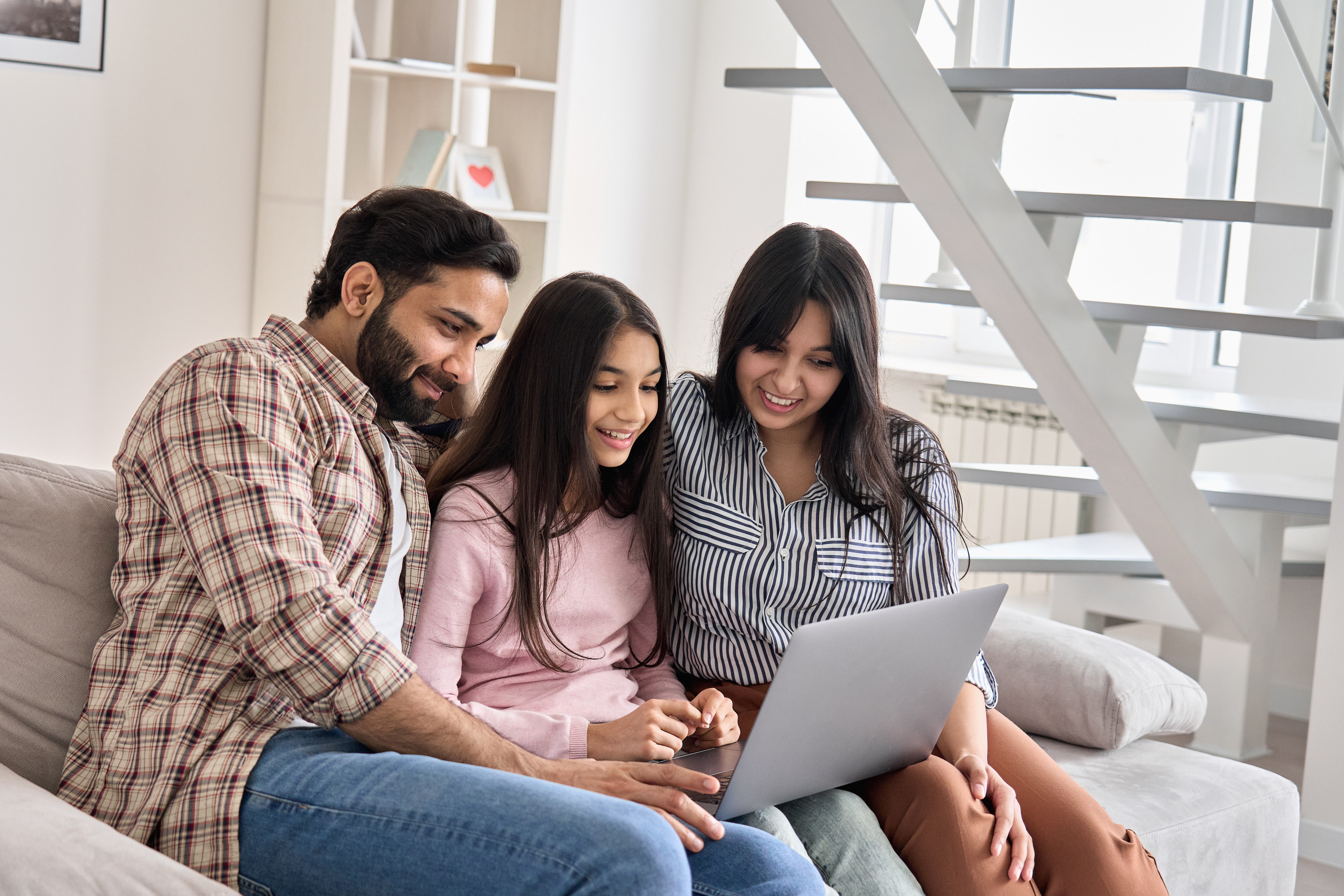 A happy family of Indian descent, with their teenage daughter, learning together on a laptop at home.