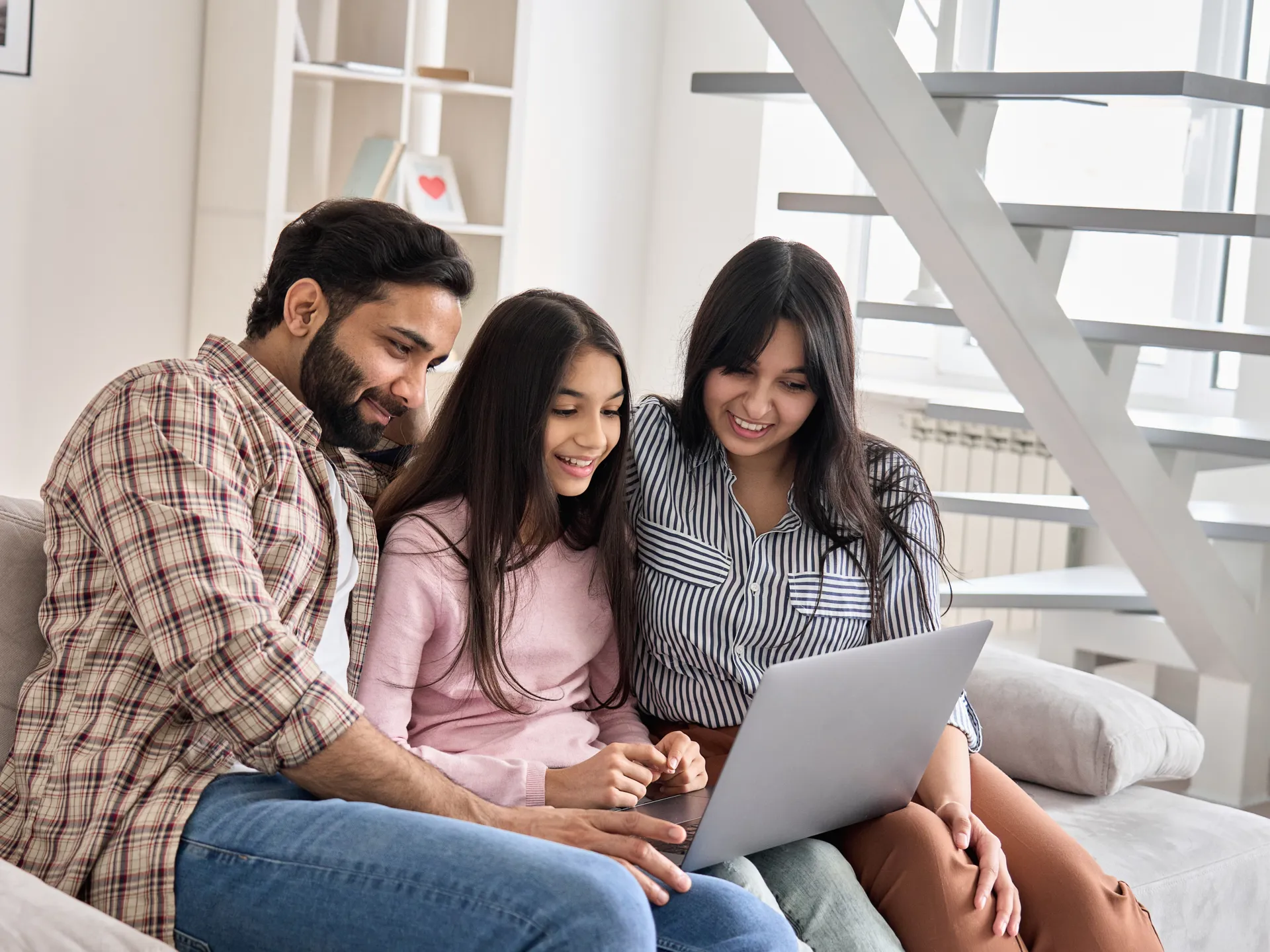 A happy family of Indian descent, with their teenage daughter, learning together on a laptop at home.