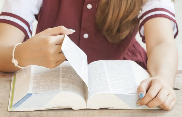 A student reading from a large book. 