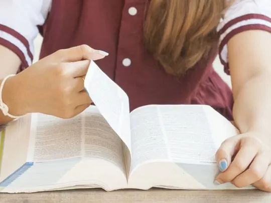 A student reading from a large book.