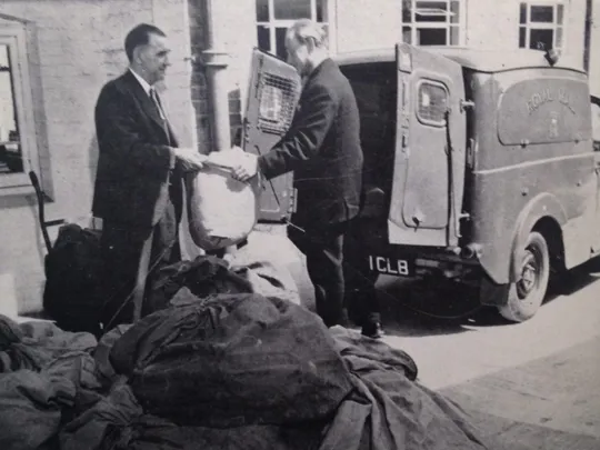 An old photograph of a Wolsey Hall Oxford employee handing correspondence course papers to a postman. The photo is taken from our 1964 prospectus, with the caption: From our 1964 prospectus: “The Post leaves Wolsey Hall. Letters and Lessons leave the College on their journey to all five continents.”