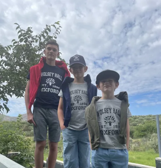 A photograph of three homeschooling young boys of different ages wearing Wolsey Hall Oxford T-shirts and smiling at the camera, representing one of our international homeschooling families.