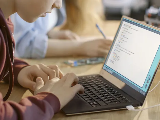 Close-up of a student typing code on a laptop, engaged in programming or computer science learning