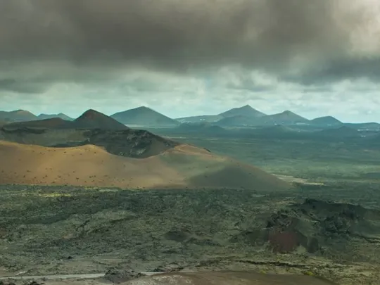 A high view of a vast landscape, with field and mountains, with a storm cloud overhead.