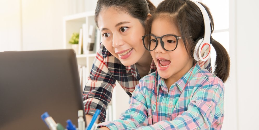 Smiling parent supporting child wearing headphones during an online lesson
