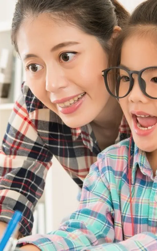 Smiling parent supporting child wearing headphones during an online lesson