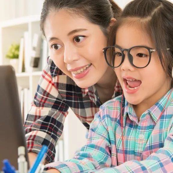 Smiling parent supporting child wearing headphones during an online lesson
