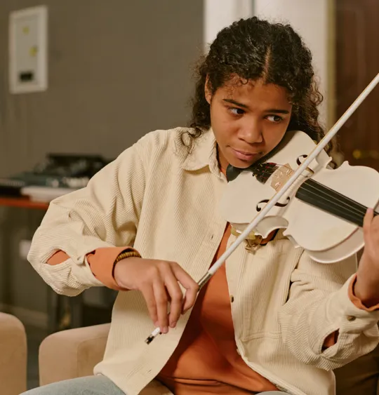 Focused teen practising the violin in a warm indoor space