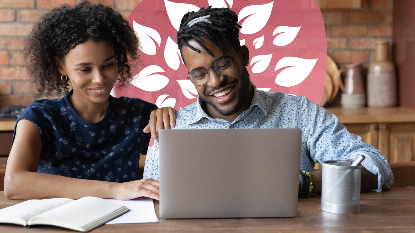 A smiling man and woman sit at a table, using a laptop and a notebook to plan their child's online education together