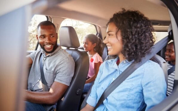 A homeschooling travelling family driving in their car. The mum and dad are smiling at each other, with their two children sitting in the back.
