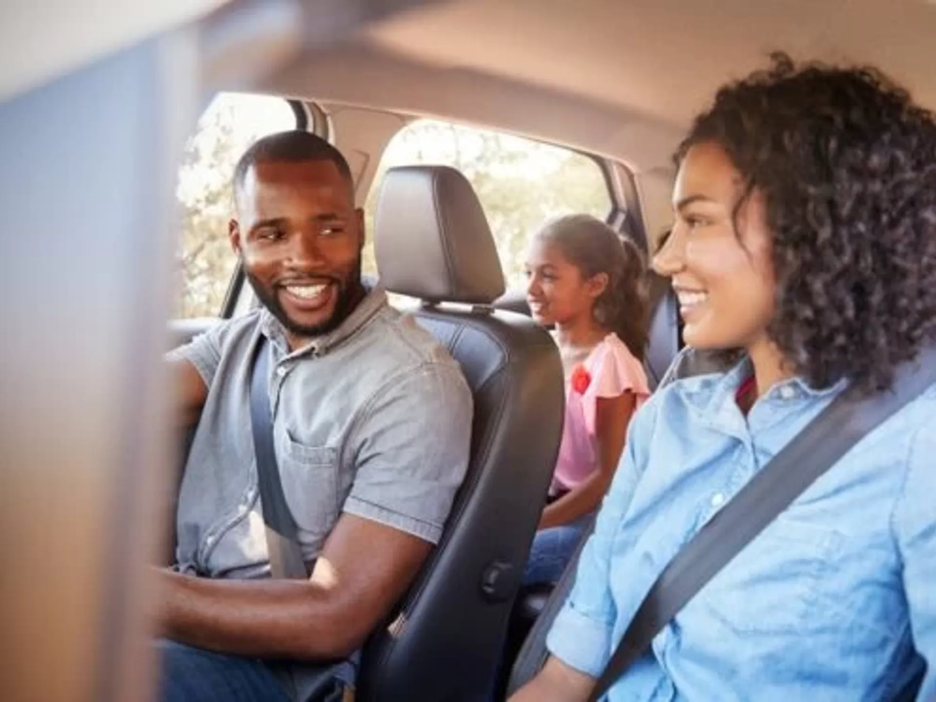 A homeschooling travelling family driving in their car. The mum and dad are smiling at each other, with their two children sitting in the back.