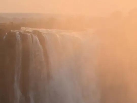 Victoria Falls in Zimbabwe with mist rising at sunset.