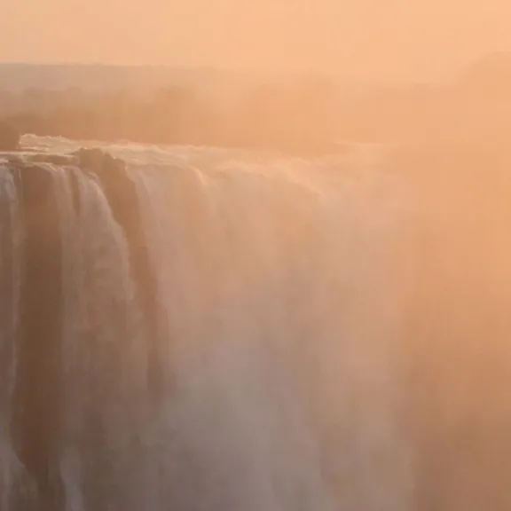Victoria Falls in Zimbabwe with mist rising at sunset.