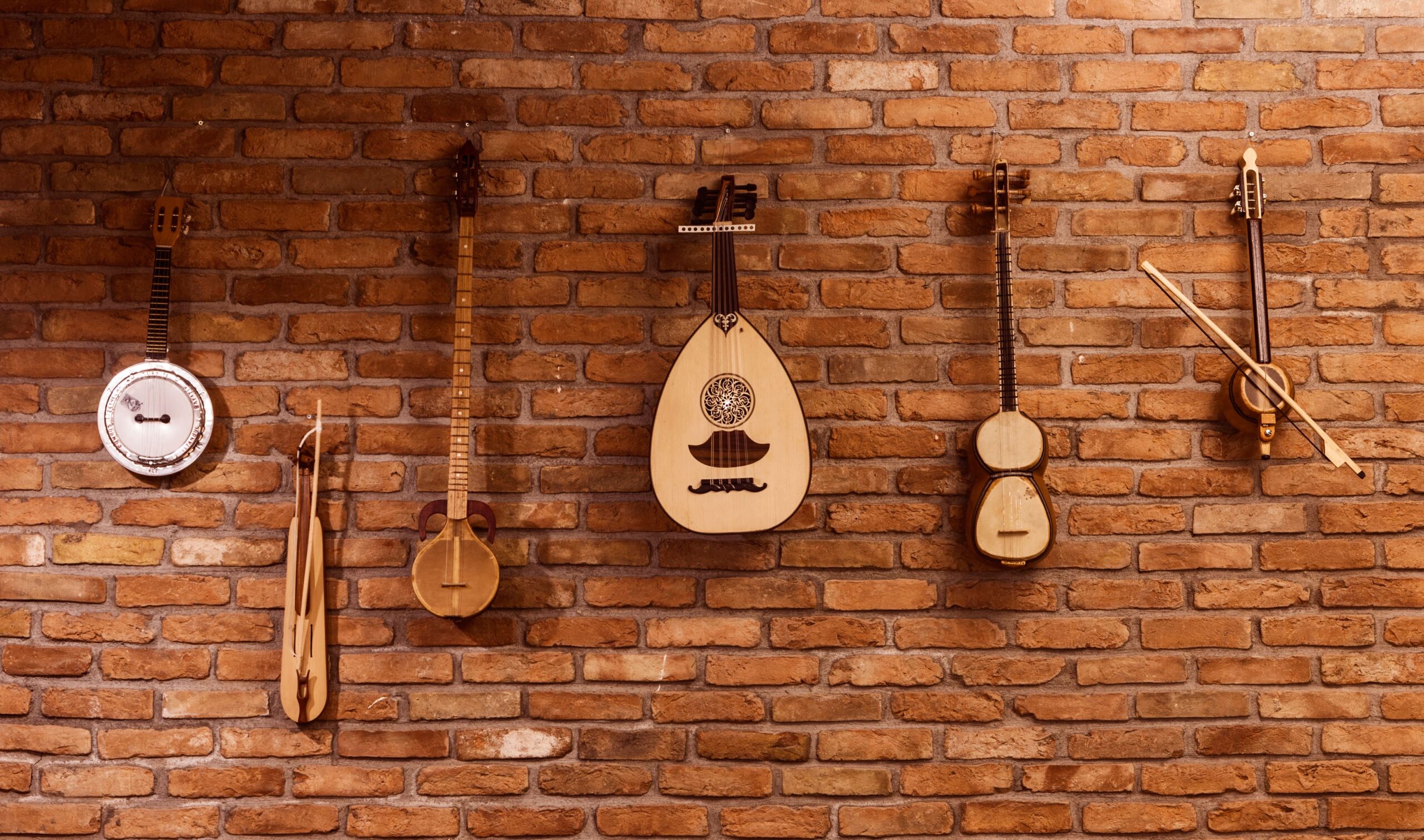 Row of traditional string instruments mounted on a rustic brick wall in a music room.