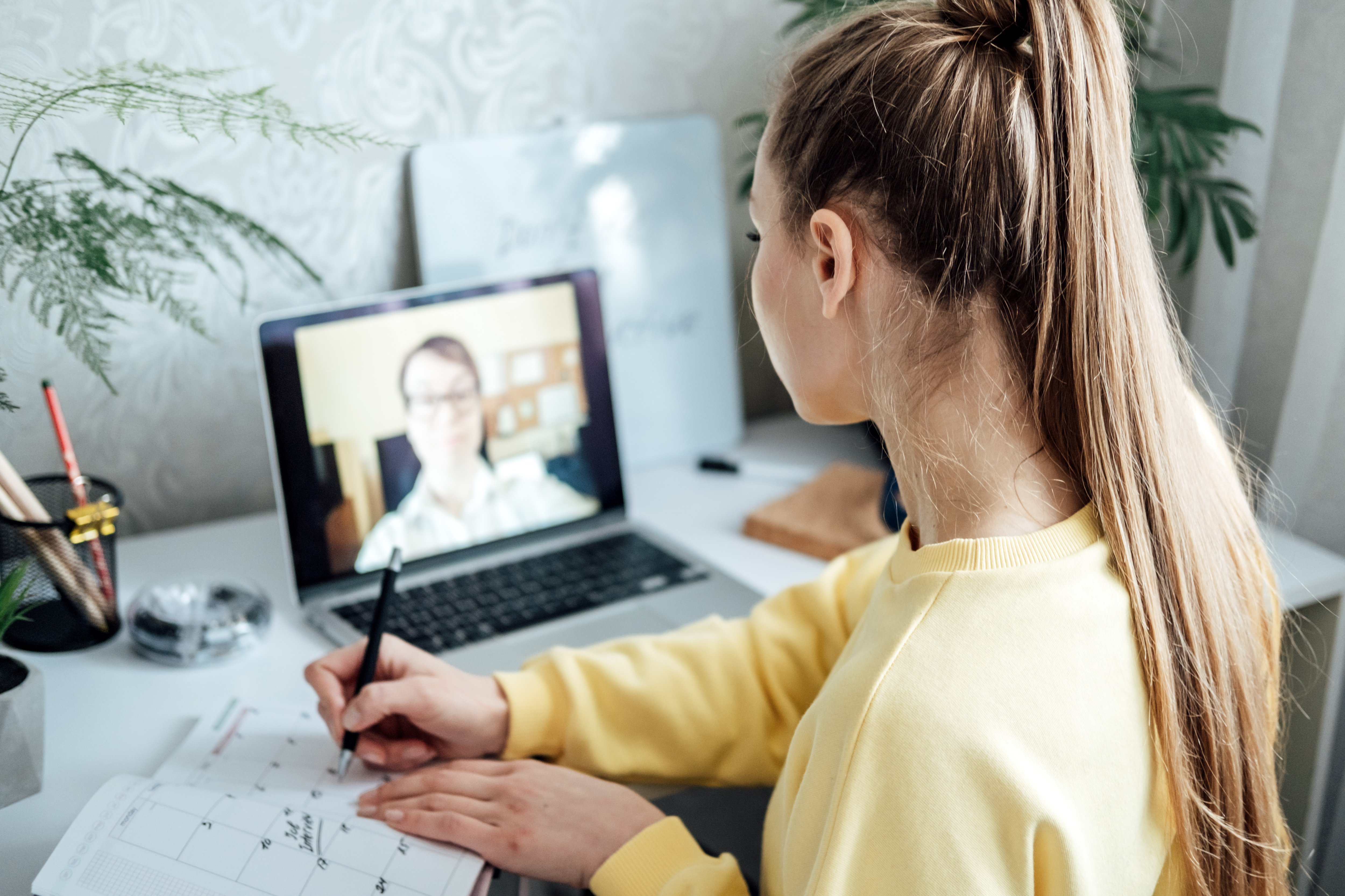 Student taking notes during a virtual lesson with a tutor on a laptop screen