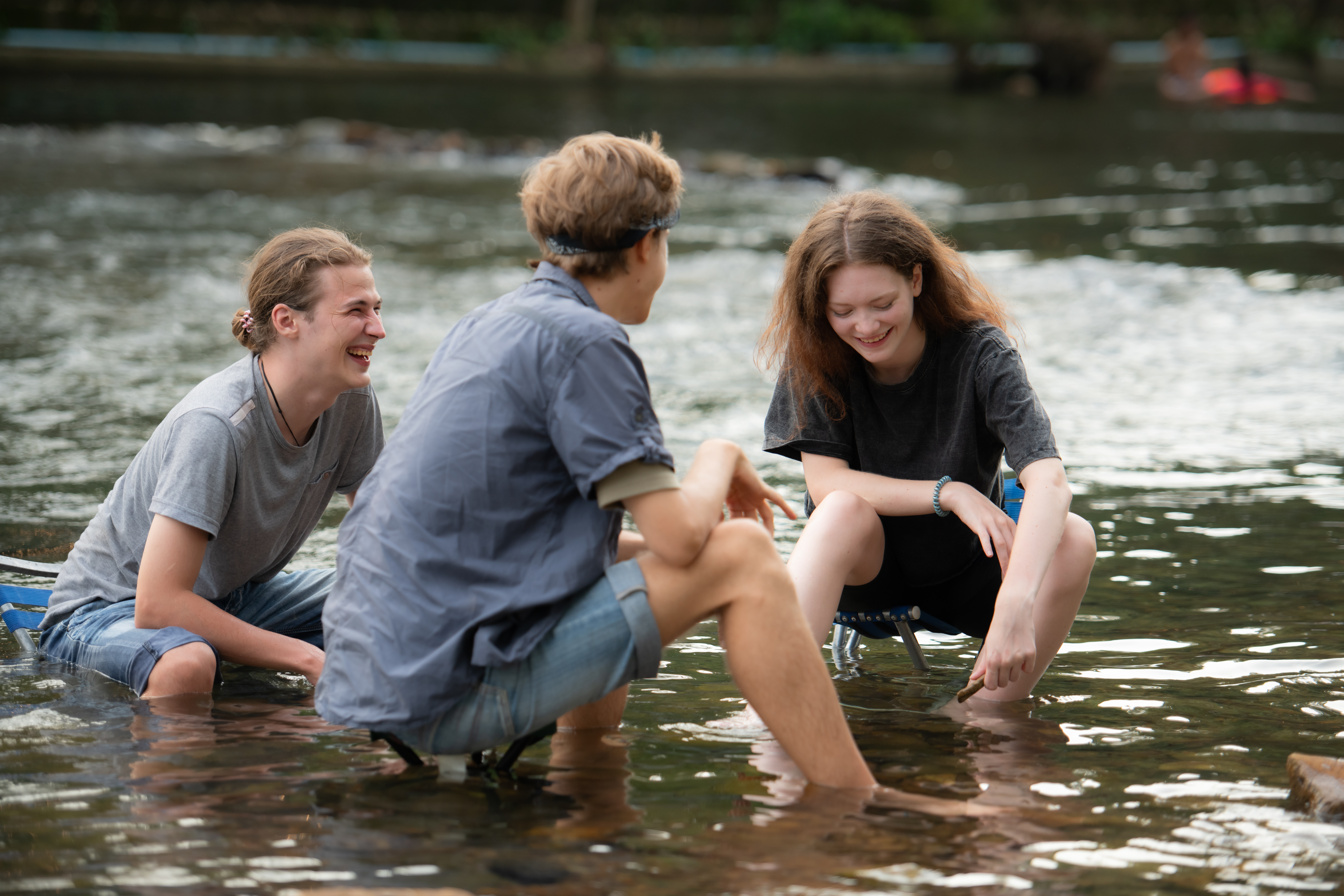 A group of friends in a shallow river inspecting marine life.