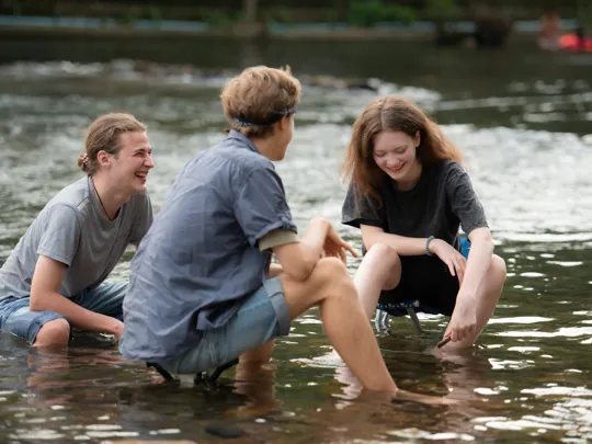 A group of friends in a shallow river inspecting marine life.