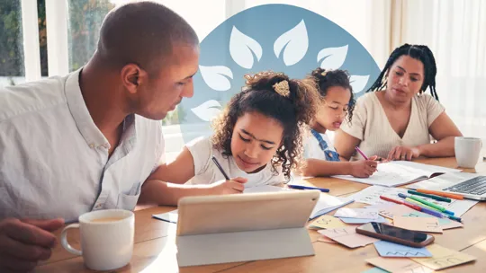 Two adults assisting two children who are writing and using a tablet at a dining table filled with study materials.
