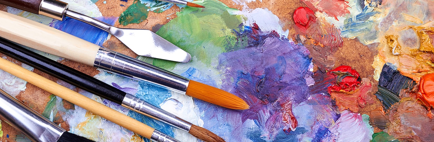 Collection of well-used paintbrushes resting on a vibrant, multicoloured artist’s palette
