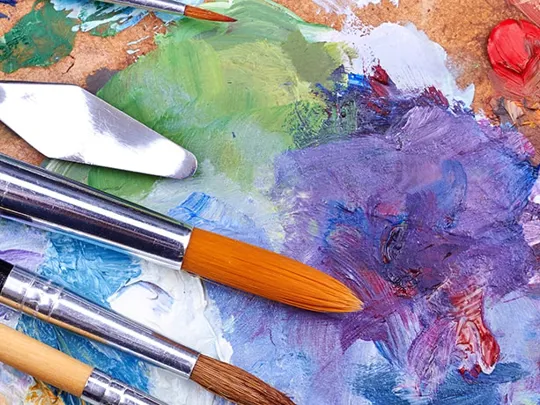 Collection of well-used paintbrushes resting on a vibrant, multicoloured artist’s palette