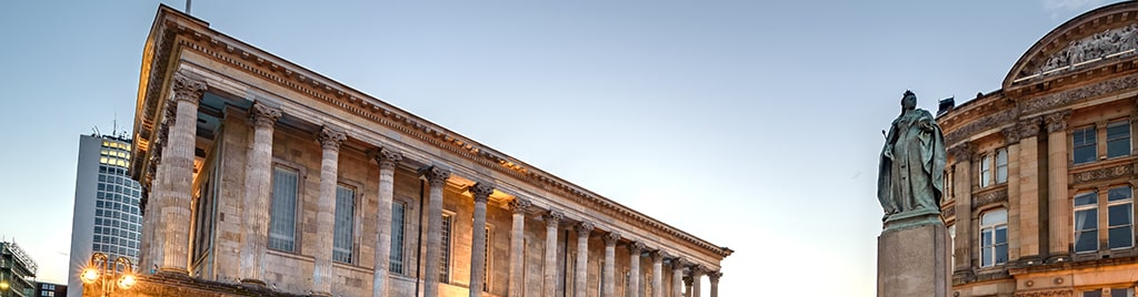 Neoclassical architecture of Birmingham Town Hall and Queen Victoria statue at dusk.