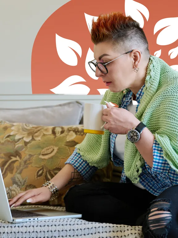 Focused parent wrapped in a blanket, holding a mug while using a laptop.