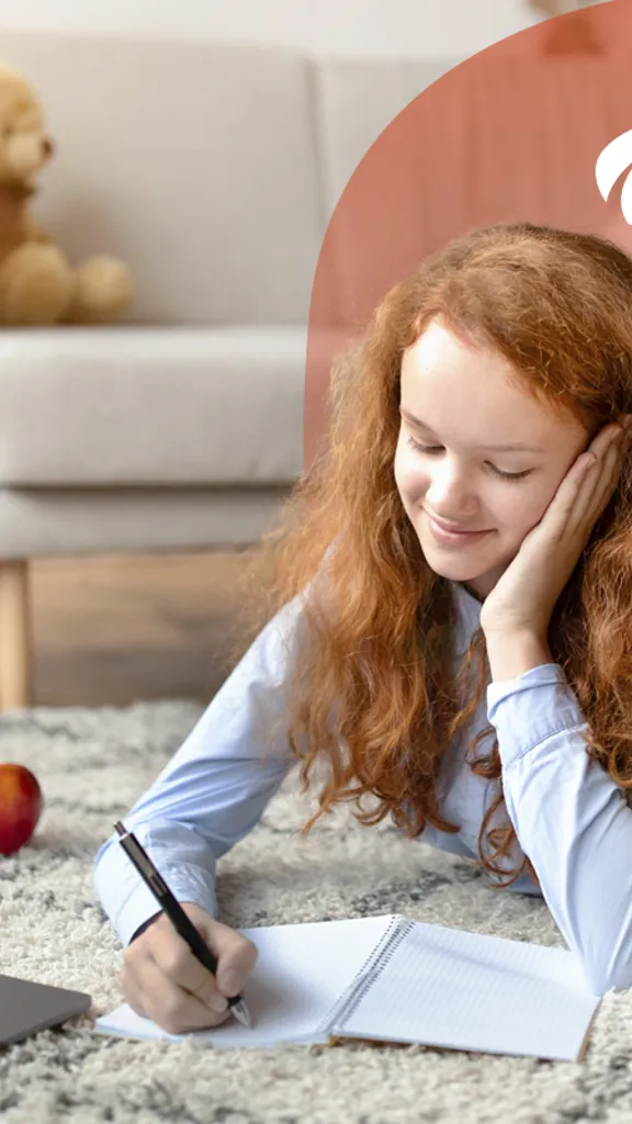 Smiling girl lying on rug, writing in a notebook with a laptop and apple nearby.