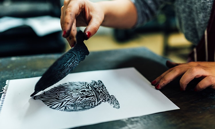 Someone creating a piece of art using ink and a stamp. 