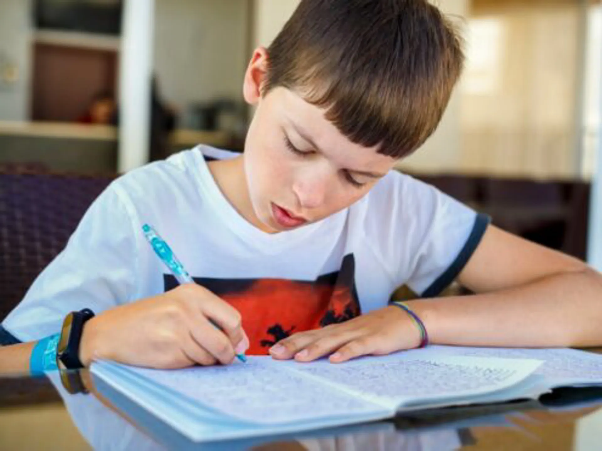 A homeschooling young boy with brown hair writing in a notepad at his desk.