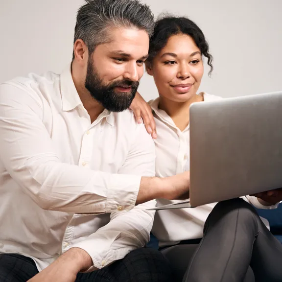 Couple seated closely on a sofa, attentively viewing a laptop screen in a relaxed home setting.