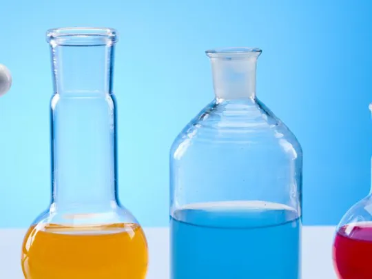 Molecular model and various glass beakers filled with coloured liquids, set against a blue background